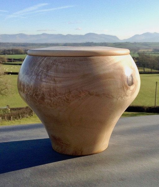 A light wooden urn that has a wide opening at the top and a smaller tapered bottom